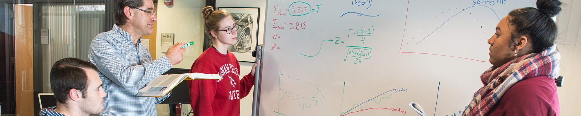 3 students and a teacher looking at a whiteboard